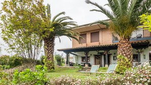 Una casa con porche cubierto, un jardín con flores y plantas, y una palmera.