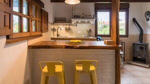 Una cocina con armarios de madera, una isla de madera con taburetes amarillos, una lámpara colgante y un estufa de leña.
