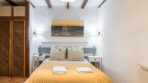 Un dormitorio con cama, dos mesitas de noche, un armario de madera y una pintura de atardecer.