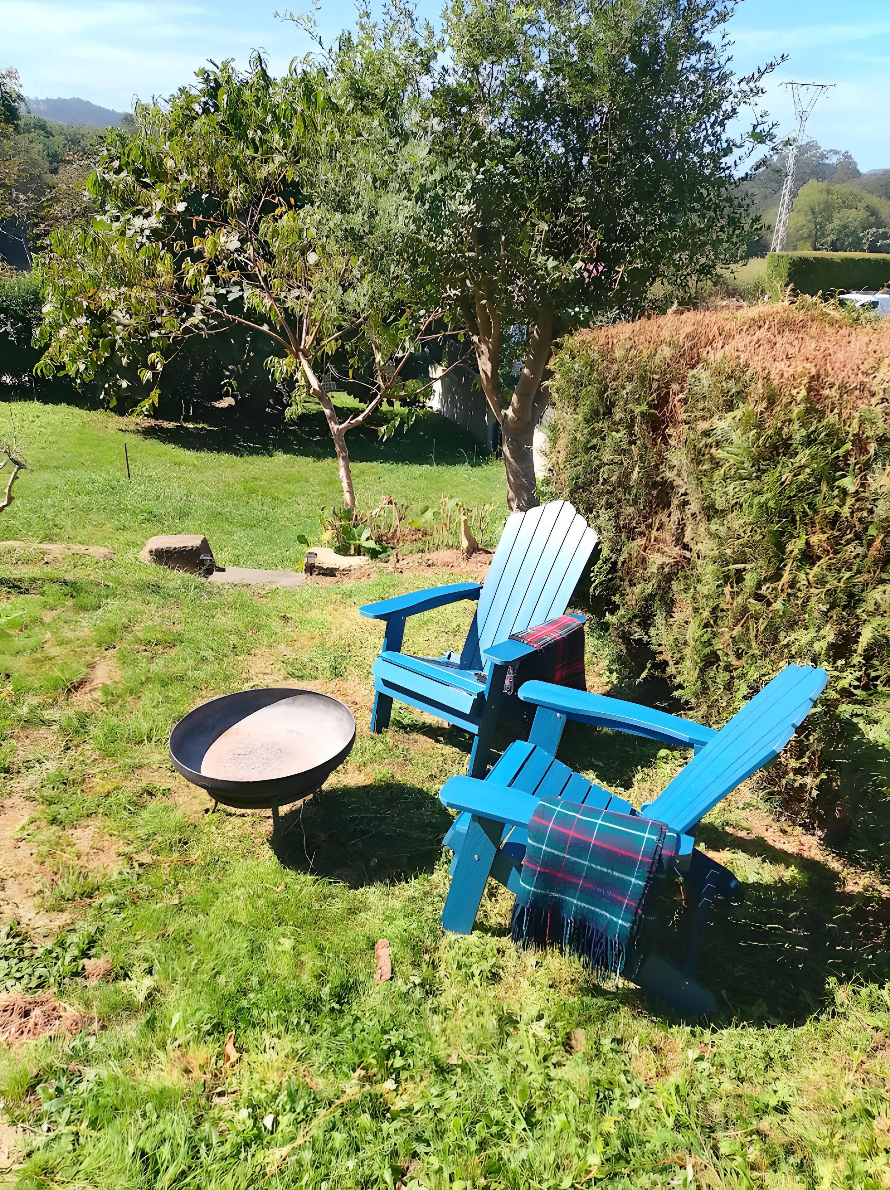Un jardín con una mesa redonda y dos sillas Adirondack azules, una con una manta a cuadros.