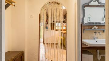 A doorway with a macrame curtain, a wooden shelf with a yellow container, and a bathroom with a white sink and mirror.