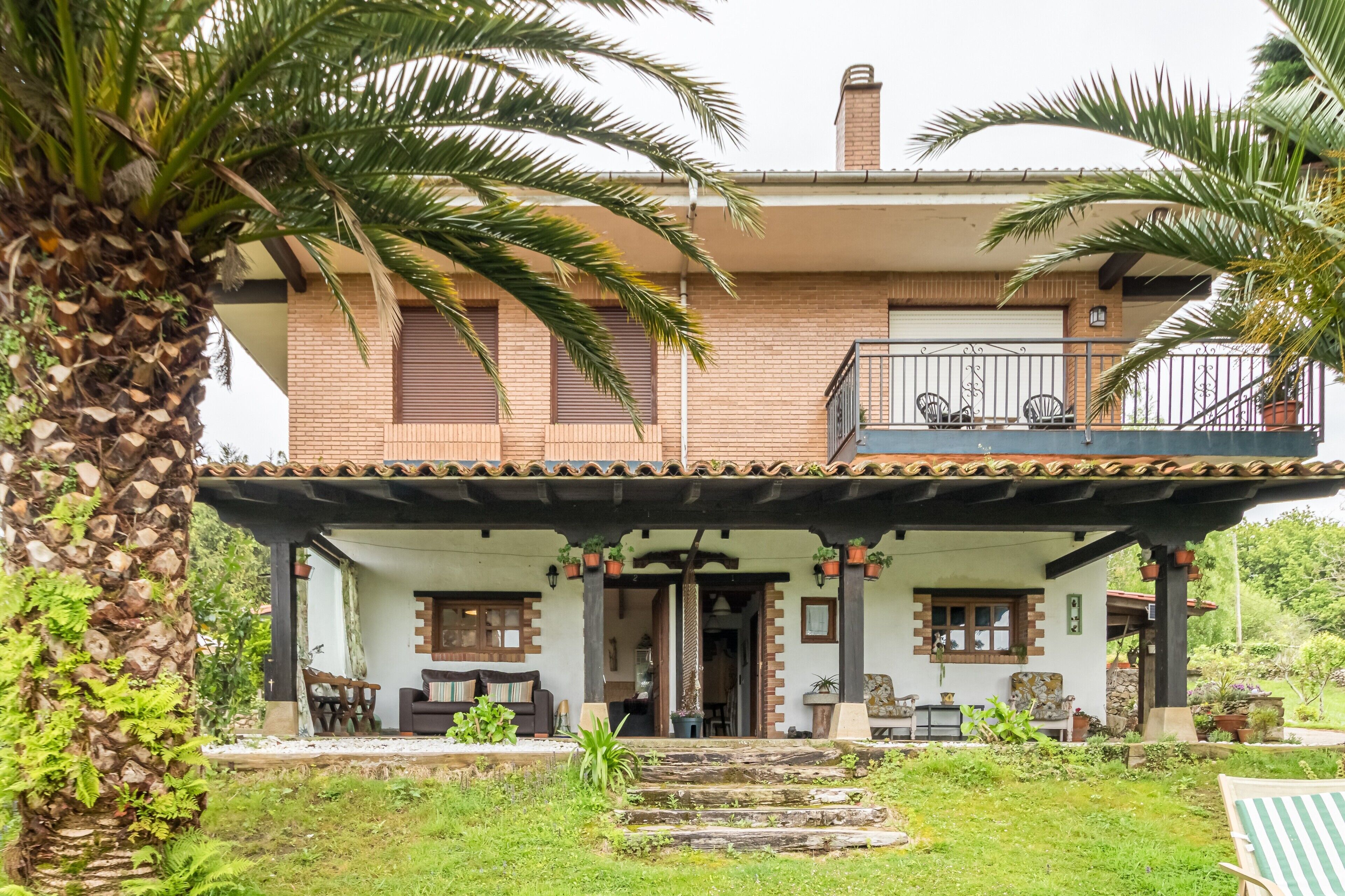 A two-story house with a covered porch, outdoor seating, and a garden.