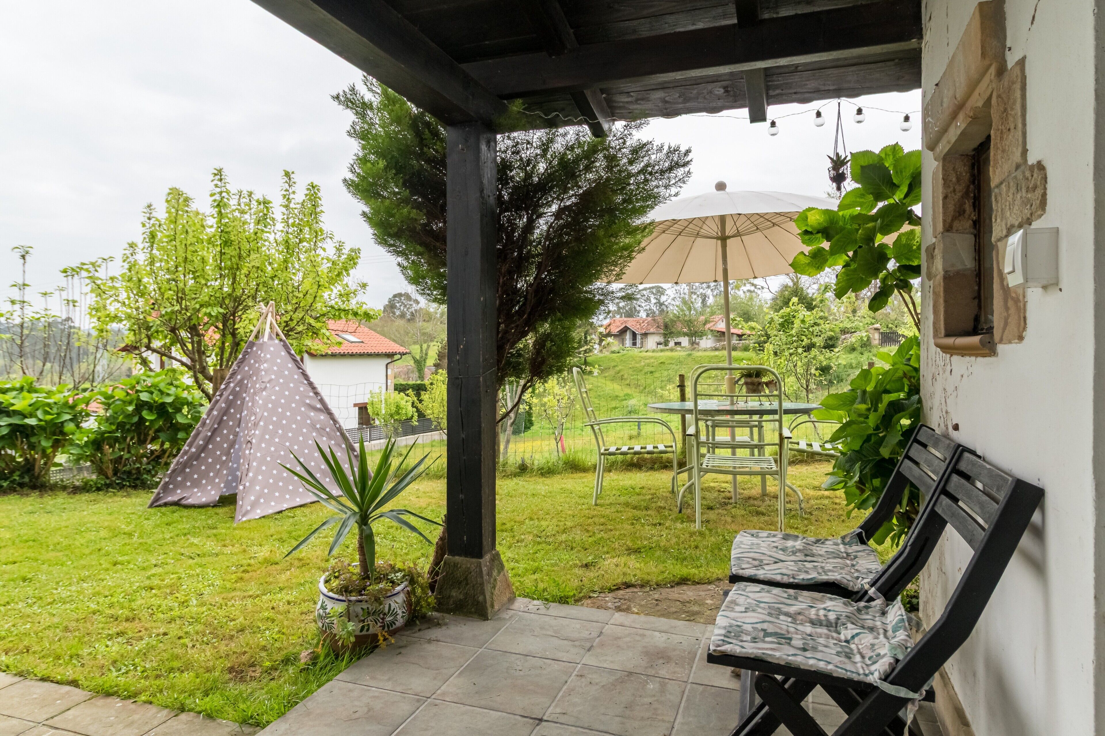 Eine überdachte Terrasse mit Tisch, Stühlen, einem kleinen Zelt und einem Blumentopf.