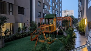 Um edifício residencial com parquinho, gramado verde e vasos de plantas.
