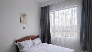 Quarto com cabeceira de madeira, uma cama de solteiro, mesa de cabeceira, obra de arte na parede e janela com cortinas.