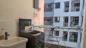 Casa de banho com lavatório, sanita e um contentor de lixo. Tem uma janela com vista para um edifício.