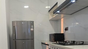 Uma cozinha compacta com geladeira de aço inoxidável, fogão a gás, armários brancos e painel de fundo de mármore.