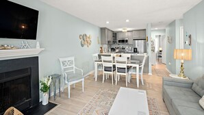 Ein modernes Wohnzimmer mit Kamin, Essbereich, Küche und Wand-Fernseher.