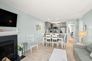 Ein modernes Wohnzimmer mit Kamin, Essbereich, Küche und Wand-Fernseher.
