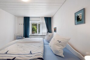 Ein Schlafzimmer mit Bett, zwei Kissen, einem Fenster mit Vorhängen, einem Heizkörper und einem an der Wand hängenden Bild.