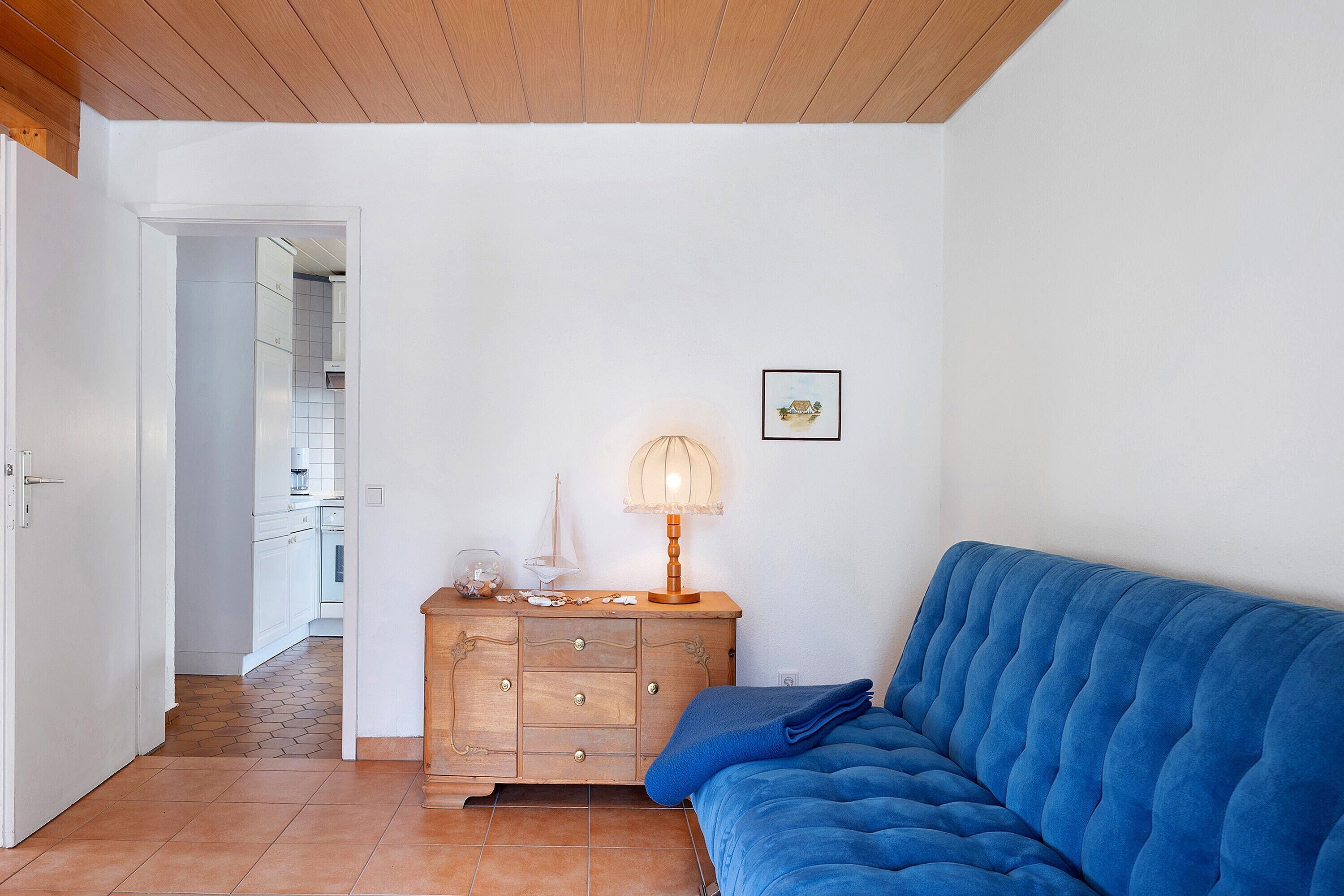 Une pièce avec un canapé bleu, une commode en bois et une lampe.