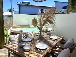 An outdoor dining area with a pool, wicker furniture, and a clear view of a modern building in the background. - Ti Cocoon by Les Ti Pêcheurs Ocean view 2 bedroom villa - swimming pool (Petite-Île)