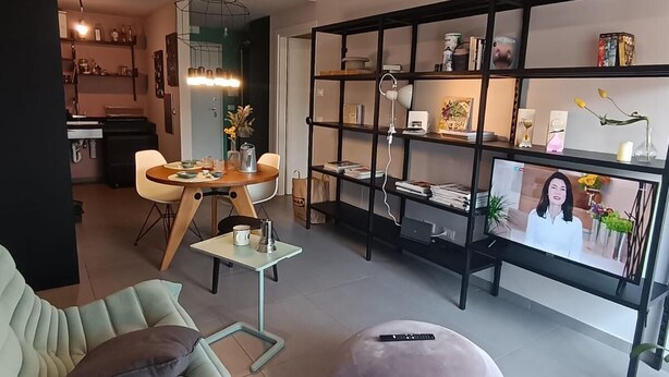 Un salon moderne avec un canapé, un pouf et un téléviseur.