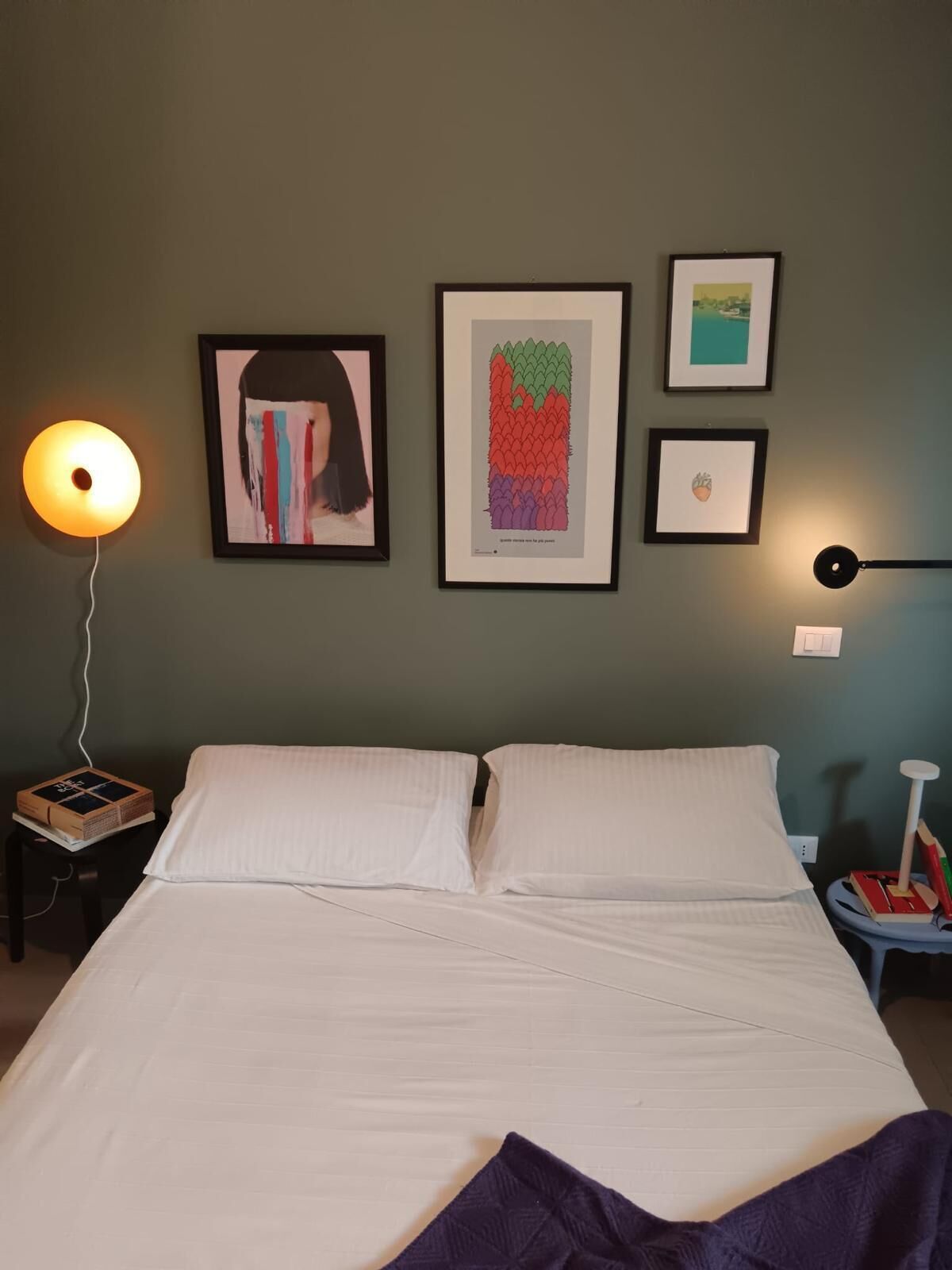 Ein ordentlich bezogenes Bett in einem Zimmer mit grüner Wand, gerahmten Bildern und Nachttischlampen.