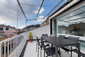 A balcony with a table and chairs, a potted plant, and a view of buildings and hills. - ‘Chiavari Elegante’ Apartment with Private Terrace, Balcony and Air Conditioning (Chiavari)