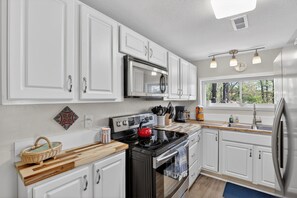 A modern kitchen with white cabinets, a stainless steel stove, a microwave, and a refrigerator.