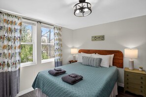 A bedroom with a bed, two bedside lamps, a nightstand, and a window with curtains.