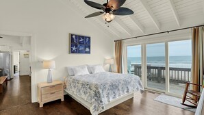 A bedroom with a large bed, a ceiling fan, a view of the ocean, and a wooden floor. - Livin' On A Prayer - Charming 3 bedroom oceanfront cottage (North Topsail Beach)