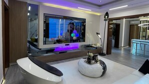 Un salon moderne doté d’un grand téléviseur à écran plat, d’un canapé blanc, d’une table basse et d’une plante décorative.