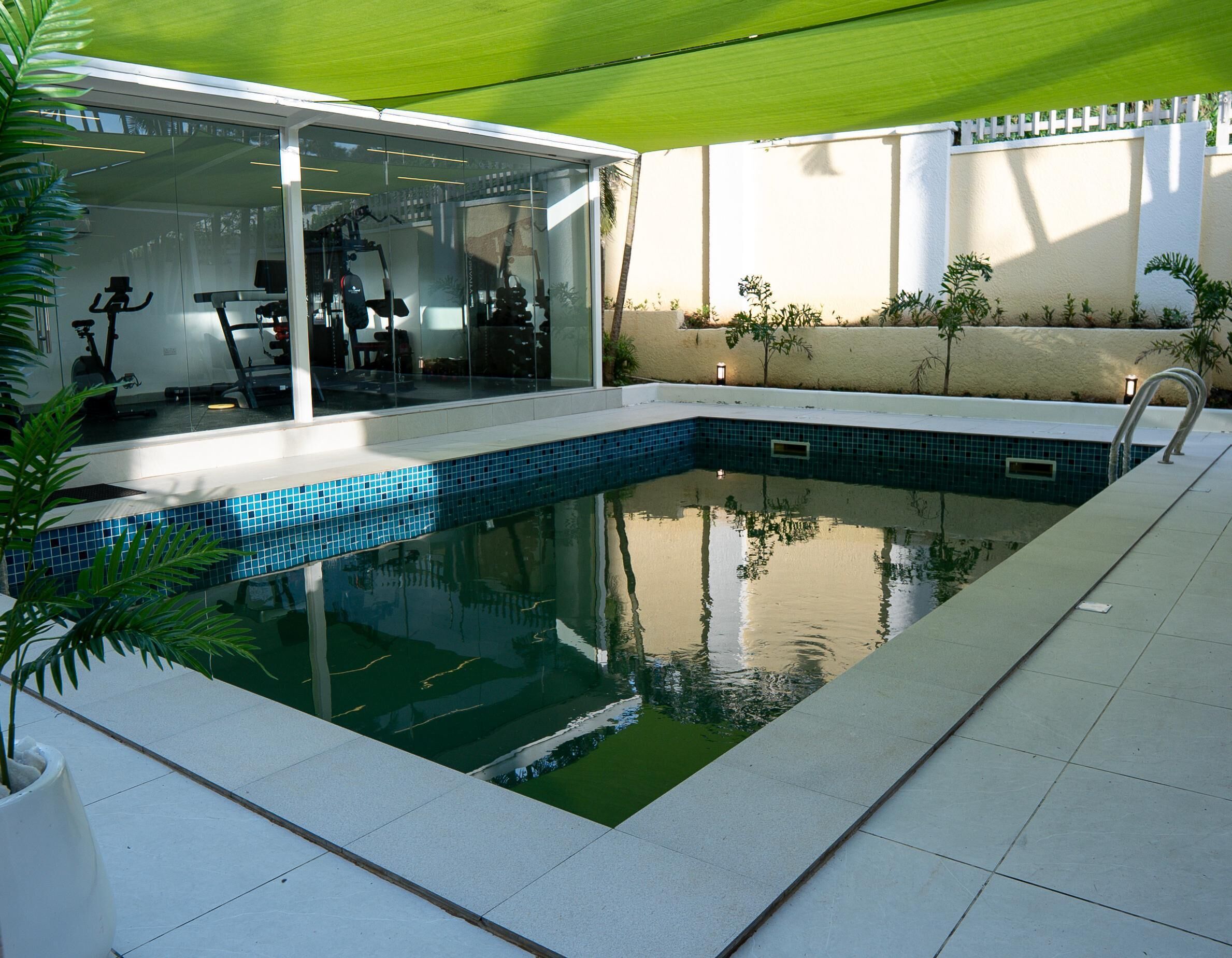 Una piscina con cerramiento de vidrio, equipo de ejercicio y plantas en macetas.