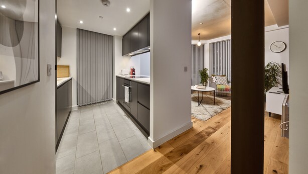 Una cucina moderna con mobili scuri, un piano di lavoro bianco e un pavimento in legno.