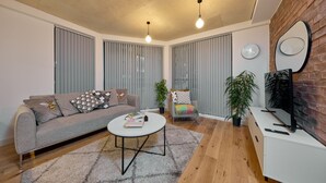 Een moderne woonkamer met een grijze bank, een ronde salontafel en een televisie op een witte kast.
