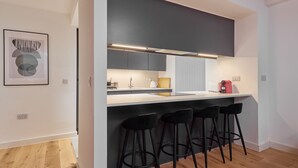 Een moderne keuken met een bar, zwarte barkrukken en een lijstwerk met kunst aan de muur.