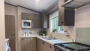 A compact kitchen with a built-in microwave, stove, oven, and a washing machine. - Beck Lodge with Hot tub (Allerthorpe)