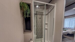 A bathroom with a glass shower enclosure, a toilet, and a small window with a plant. - Beck Lodge with Hot tub (Allerthorpe)