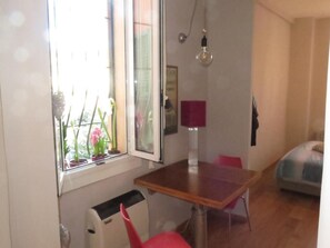 Ein Zimmer mit Fenster, Tisch, Stuhl, Lampe und Heizung.