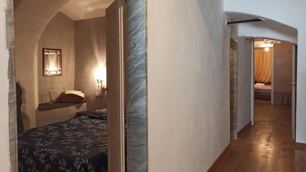 Ein schmaler Flur mit einem Bett links und einem Durchgang zu einem weiteren Zimmer.