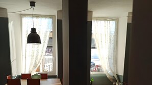Ein Essbereich mit Holztisch und Stühlen, einer Hängelampe und Blick durch ein Fenster mit durchsichtigen Vorhängen.