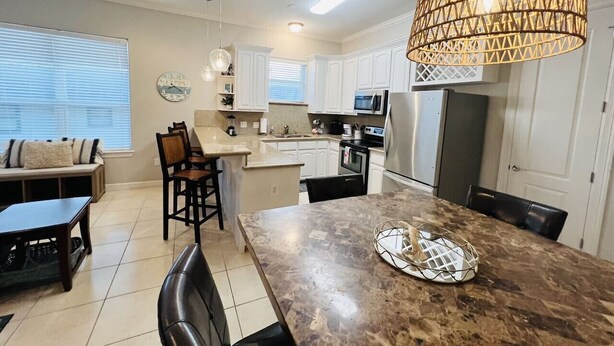 A modern kitchen with white cabinets, a granite countertop, and a hanging light fixture. - Beach Access & Poolside Patio! Easter Special! (South Padre Island)