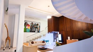 A modern interior with a staircase, a reception desk, and a giraffe sculpture. - Peravi Suites at The Essence (Accra)