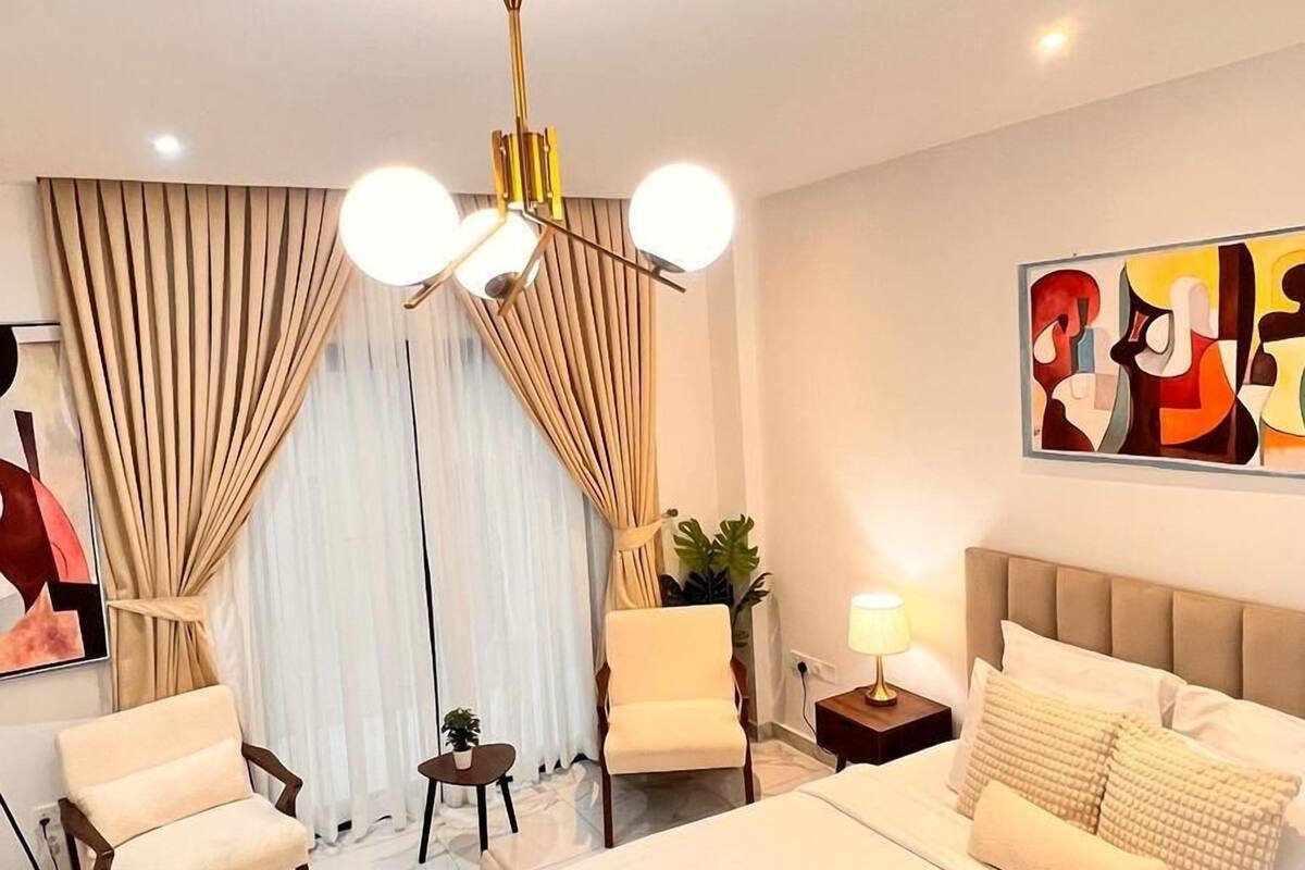Una camera d'albergo moderna con un letto, due poltrone, un comodino, una lampada e una luce a soffitto.