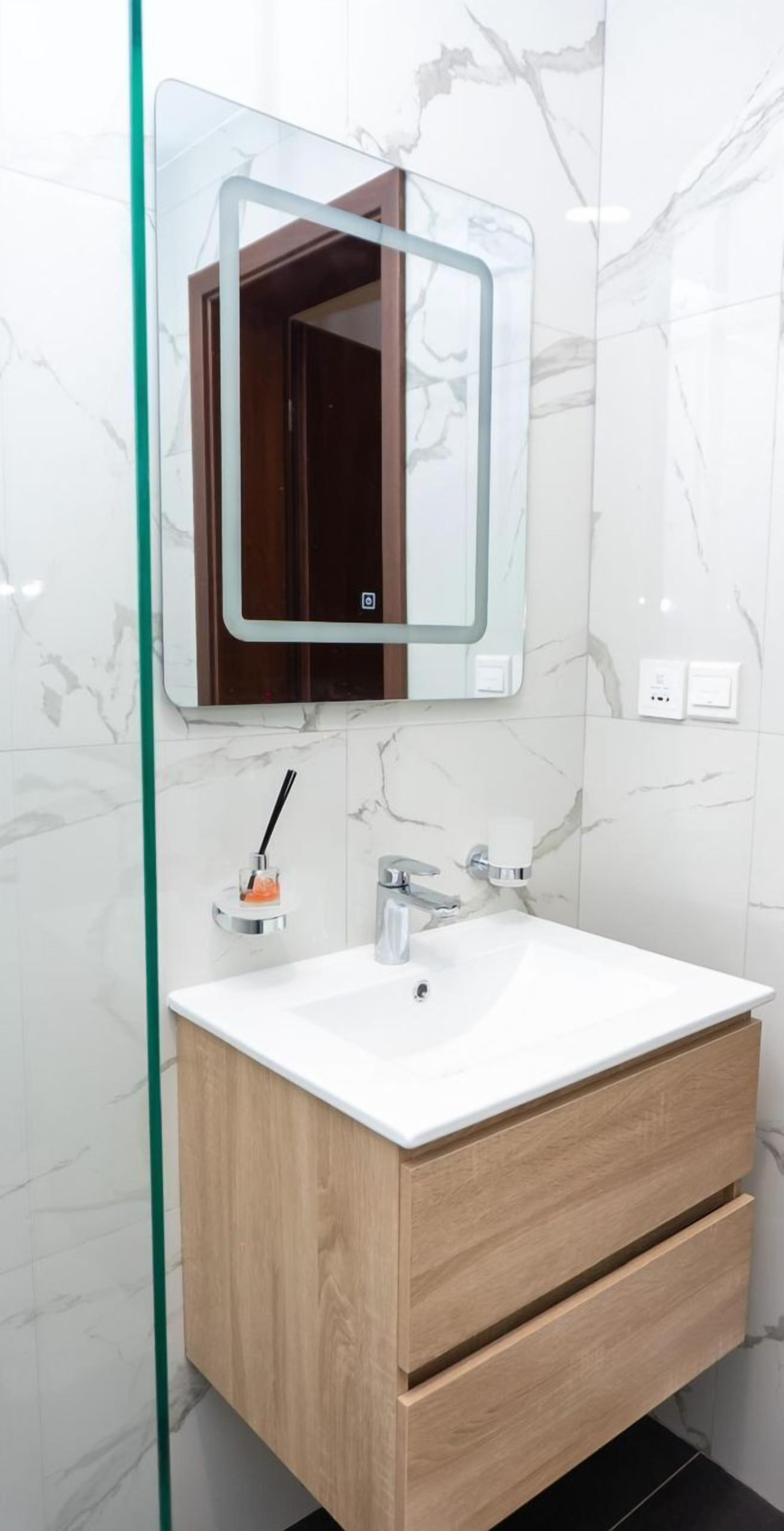 Een badkamer met een witte marmeren wand, een houten wastafelmeubel met een witte wasbak en een spiegel met houten lijst.