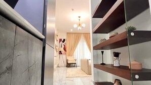A modern interior with a marble floor, a glass shelf unit, and a dining area with a chair and table. - Peravi Suites at The Essence (Accra)