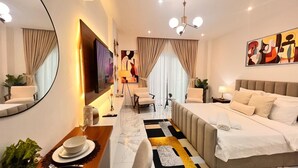 A modern hotel room with a large bed, a seating area with chairs, a dining table, and a large mirror. - Peravi Suites at The Essence (Accra)