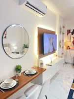 Una sala de estar moderna con un televisor de pantalla plana, un espejo redondo, una mesa consola de madera y un suelo de mármol.