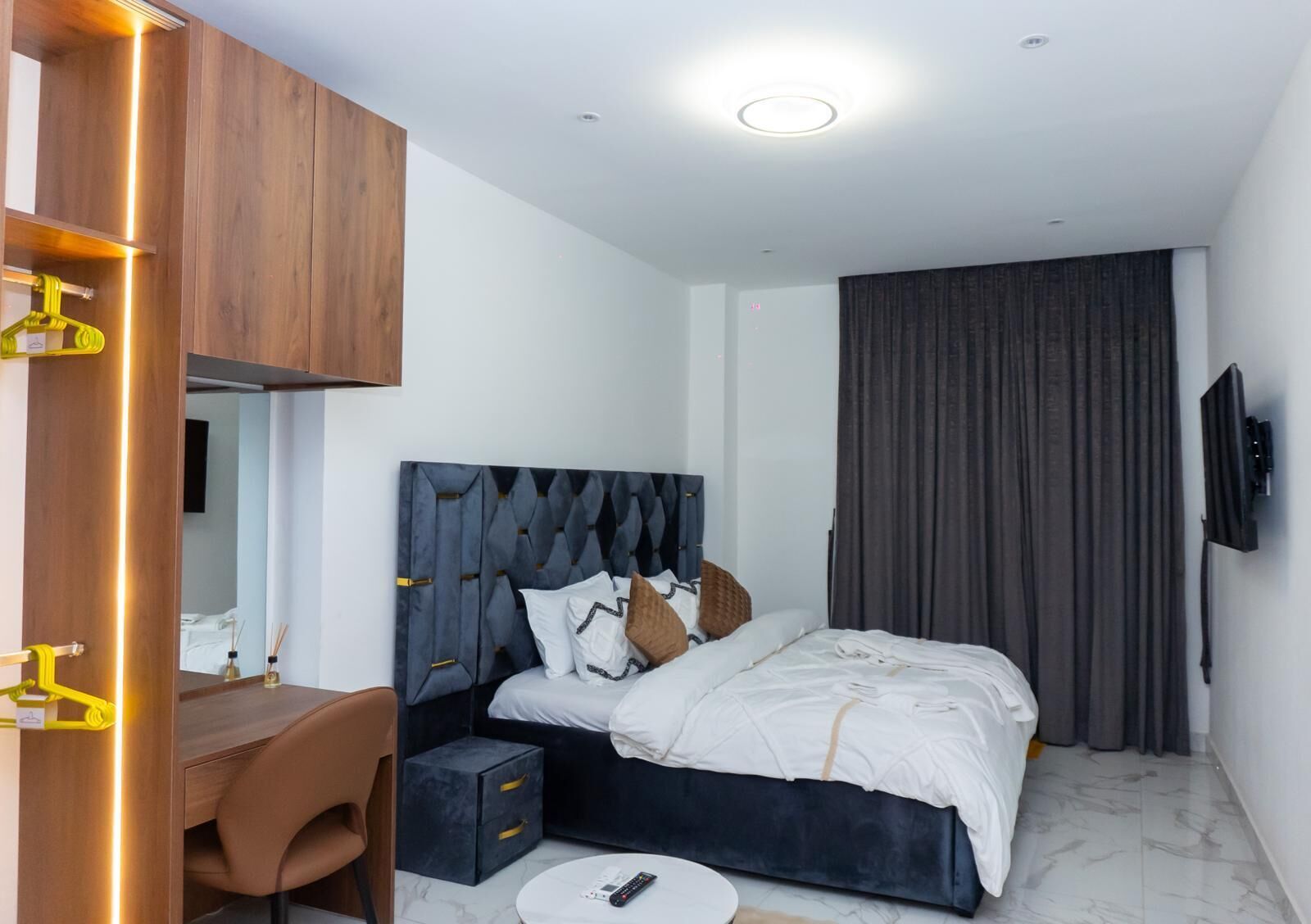 Ein modernes Schlafzimmer mit Bett, Nachttisch, Sessel und einem an der Wand befestigten Fernseher.