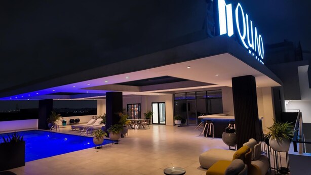 A modern indoor pool area with a bar and seating, large windows, and a poolside lounge. - Peravi Suites at The Essence (Accra)