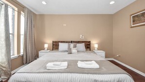 Una habitación de hotel con una cama grande, dos mesitas de noche con lámparas, una ventana con cortinas y un cuadro en la pared.