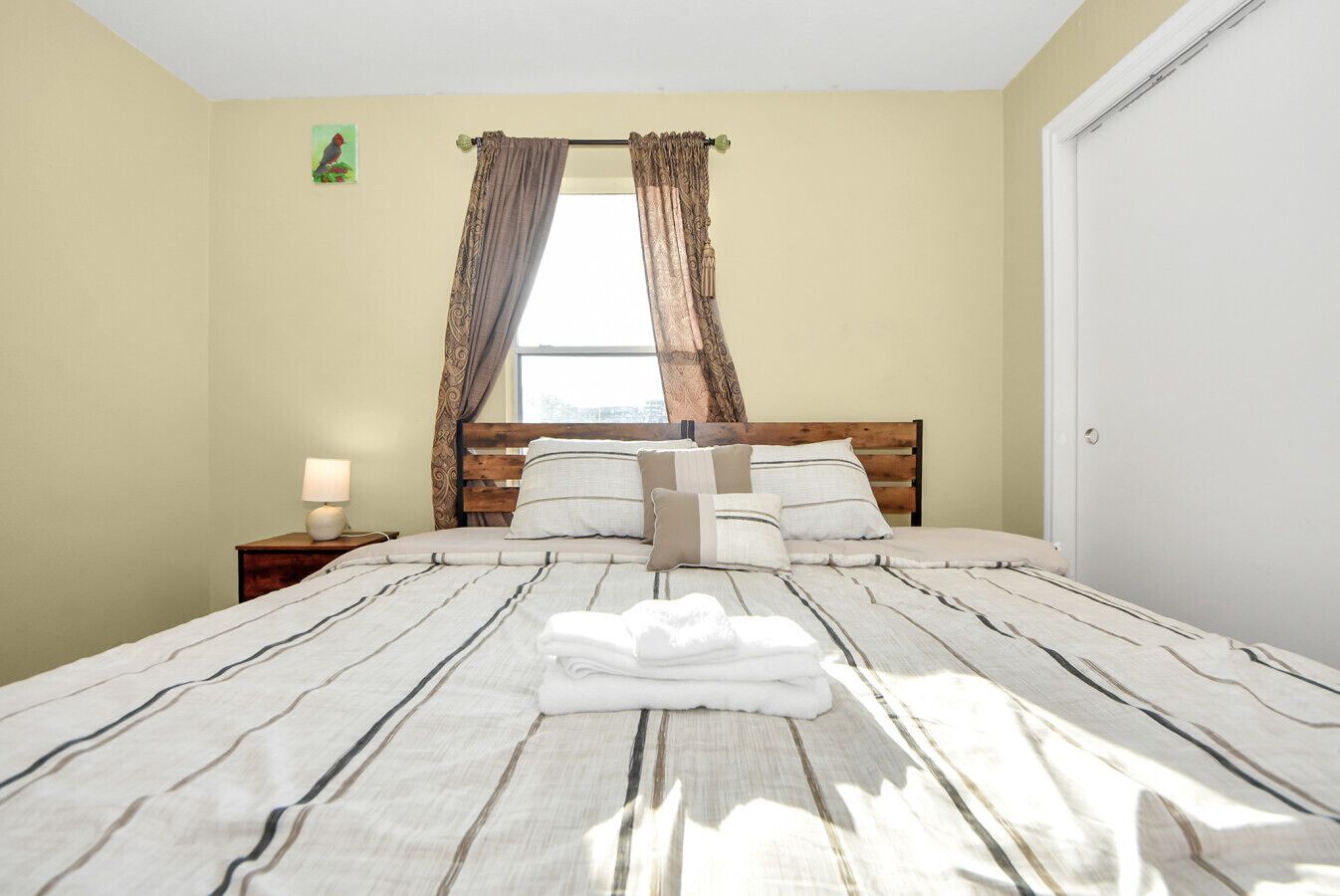Un letto rifatto con lenzuola a righe, una testiera in legno e un comodino con una lampada.