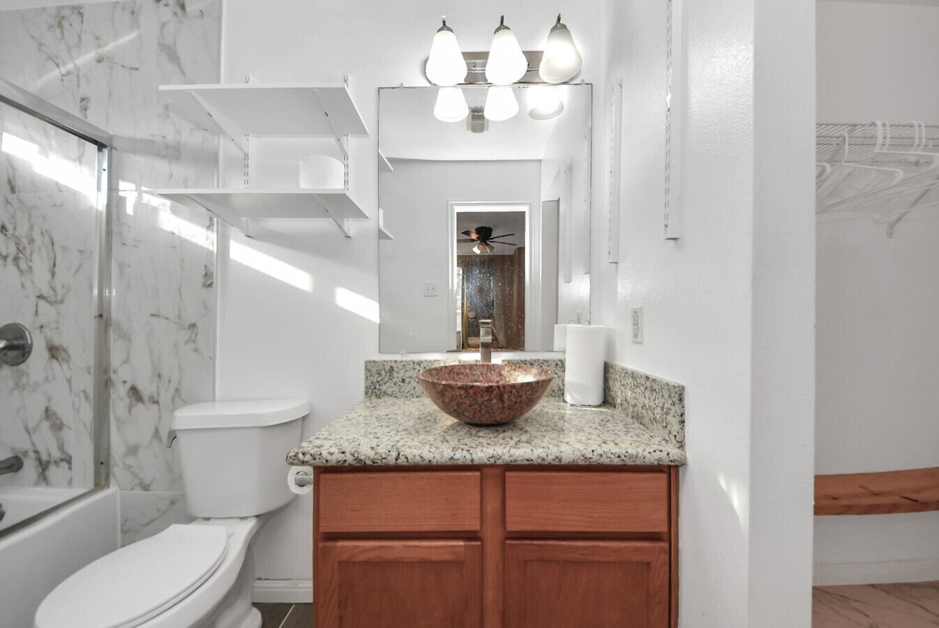 A bathroom with a marble shower, a sink with a copper bowl, and wooden cabinets.