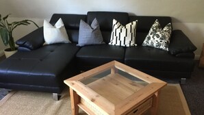 Ein Wohnzimmer mit einem Ecksofa, einem Couchtisch mit Glasplatte und einem gewebten Teppich.