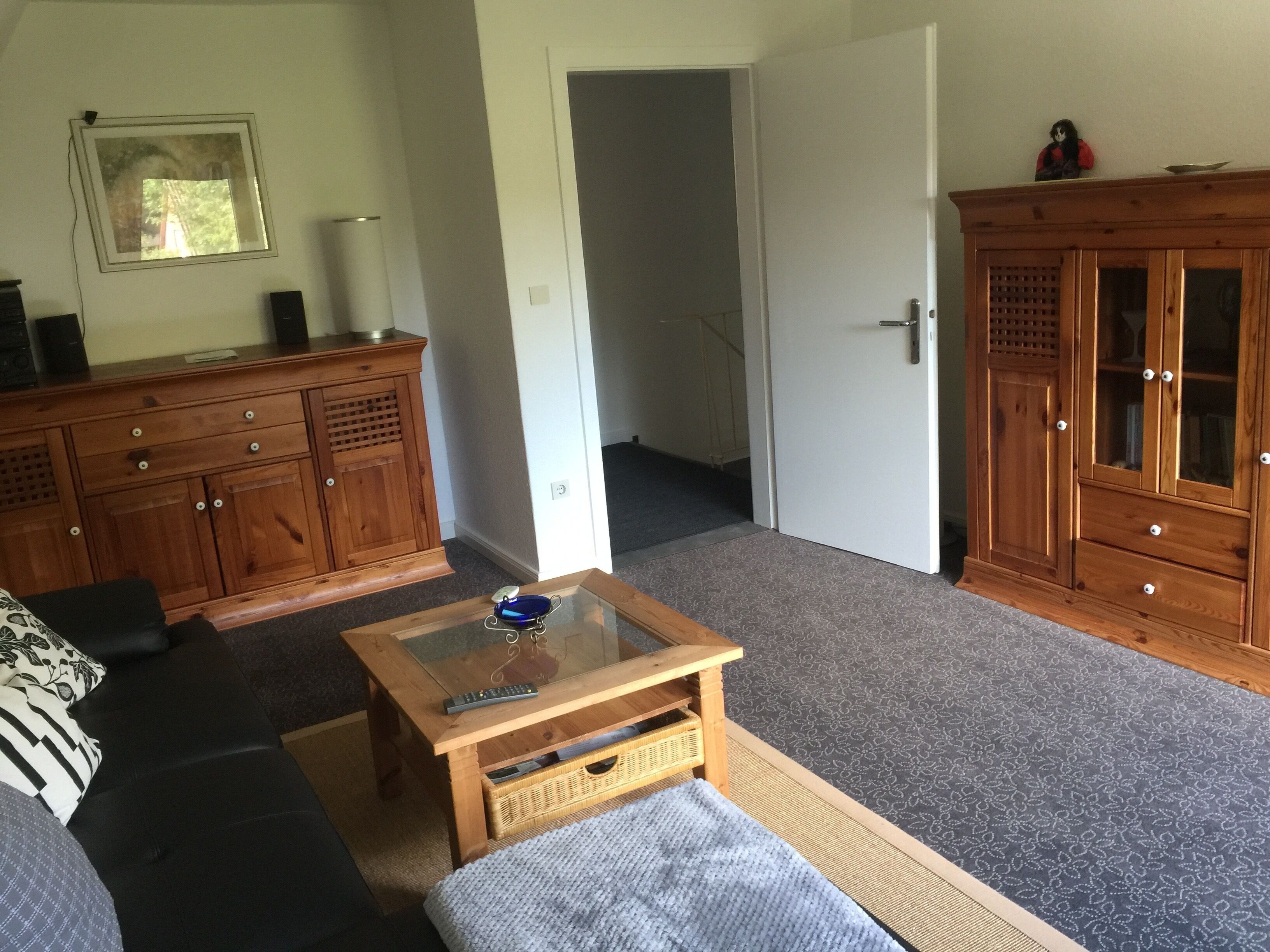 Ein Wohnzimmer mit einer Couch, einem Glastisch, einem Holzschrank und einer Tür zu einem anderen Raum.