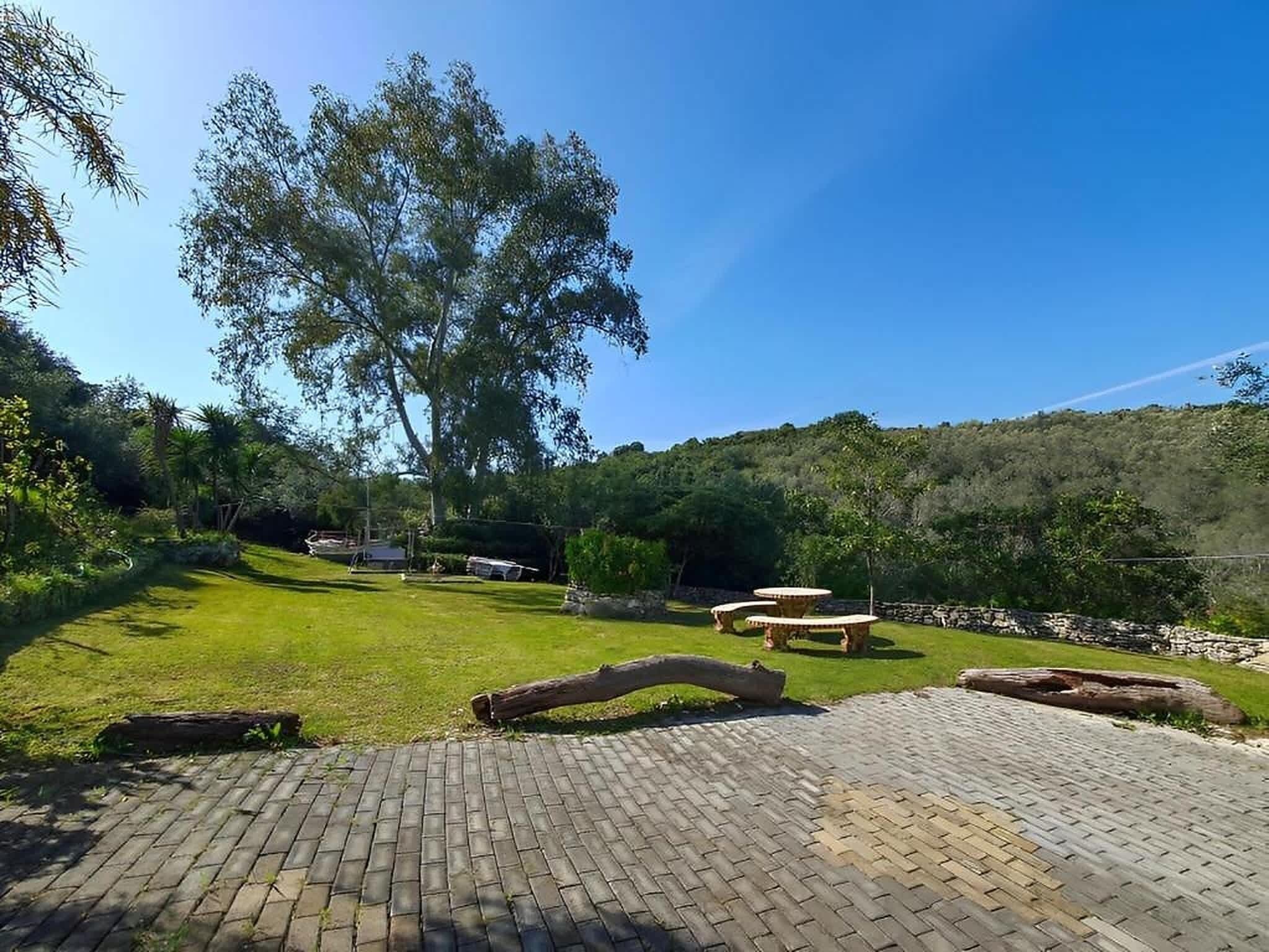 Un patio empedrado con césped, un árbol grande y un muro de piedra al fondo.