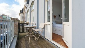 A balcony with a table and chairs, a bed, and a view of the city. - Noordzee Apartment 2 (Zandvoort)