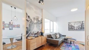 A modern living room with a glass dining table, a sofa, a coffee table, and a large window. - Noordzee Apartment 2 (Zandvoort)