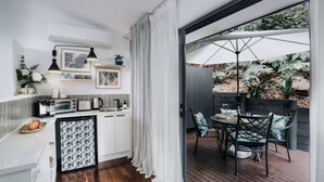 Una cocina moderna con armarios blancos, un comedor con mesa y sillas, y vista a un jardín por una puerta corrediza.